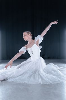 Ballerina in a graceful pose wearing a classic white dress in a studio setting.