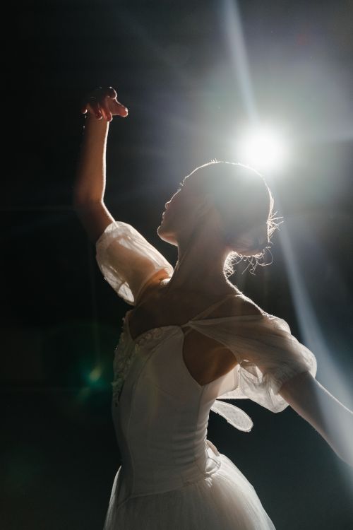 Free Silhouette of a ballet dancer in a white costume gracefully posing under spotlight. Stock Photo