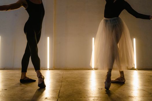 Two ballet dancers practicing graceful poses in a dimly lit dance studio.