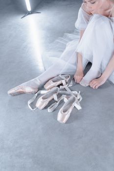 Ballet dancer sitting on studio floor adjusting pointe shoes. Professional and graceful.