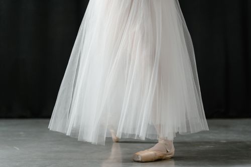 Free Close-up of a ballerina's feet in pointe shoes wearing a flowing white dress. Stock Photo