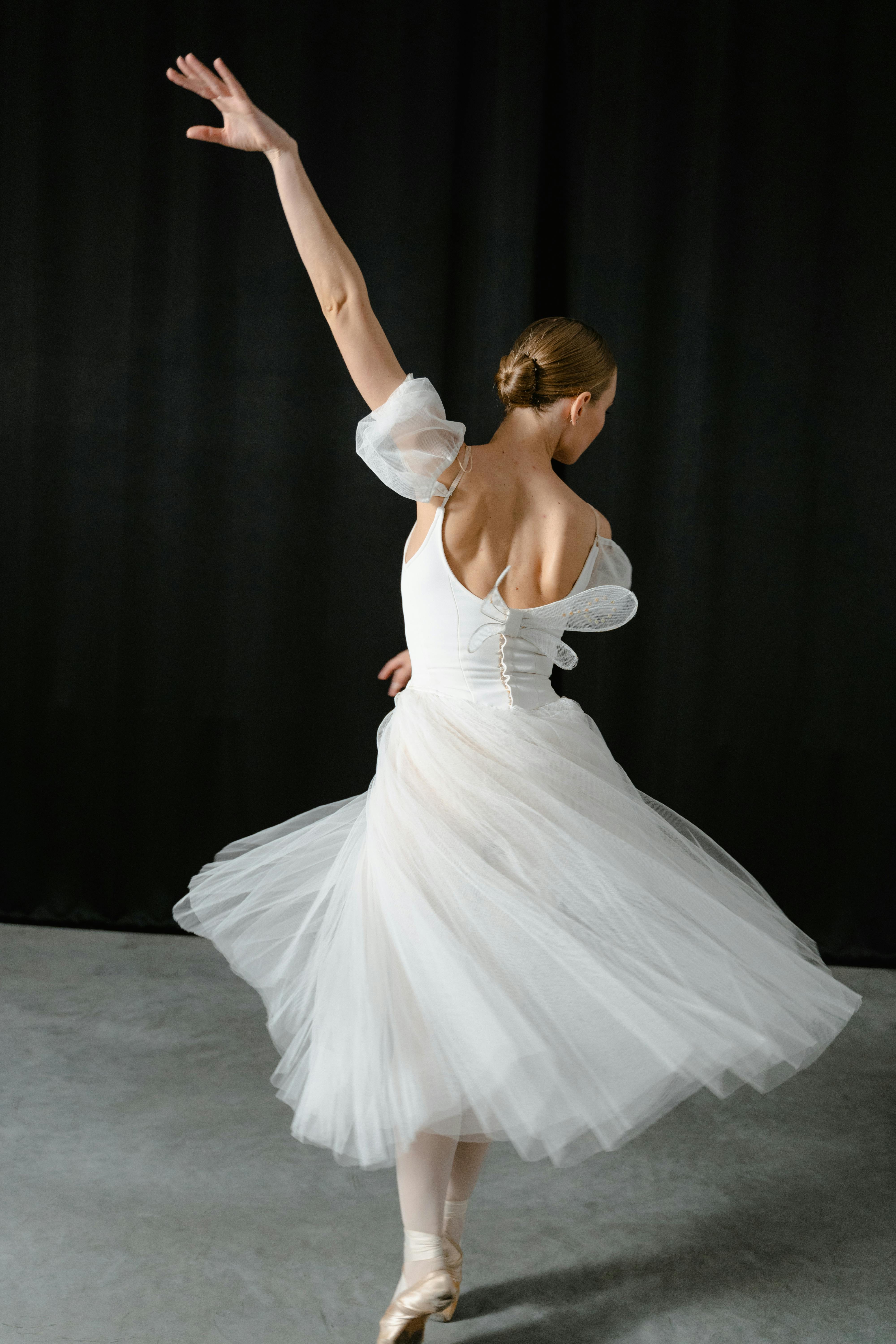 Free Graceful ballerina in a flowing white dress performing in a studio setting. Stock Photo