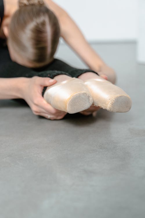 A Ballerina Sitting on the Floor while Stretching Her Legs