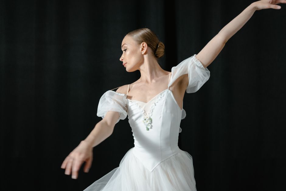 Graceful ballerina in white tutu performing dance on stage against a black backdrop.