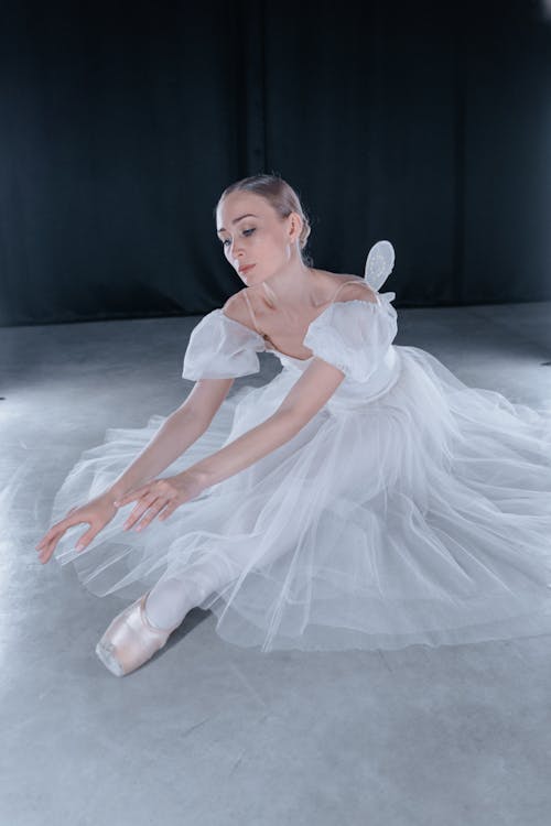 A Ballerina in White Tutu Dress Sitting on the Floor 
