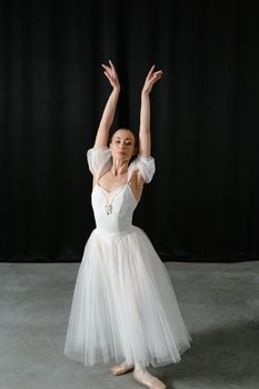 Elegant female ballet dancer in a classic white tutu performing in a studio.