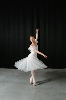 Ballerina in a white tutu gracefully posing indoors during a ballet rehearsal.