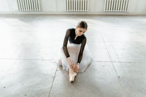 Free A graceful ballerina adjusts her pointe shoe, preparing for a dance rehearsal in a bright studio. Stock Photo