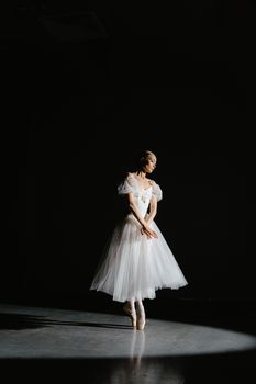 A graceful ballerina in a white dress performing under a spotlight on stage, showcasing poise and elegance.