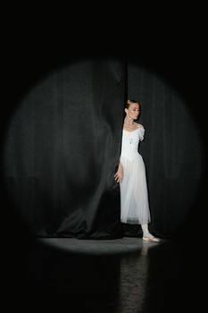 A graceful ballerina in a white dress peeks from behind the theater curtain.