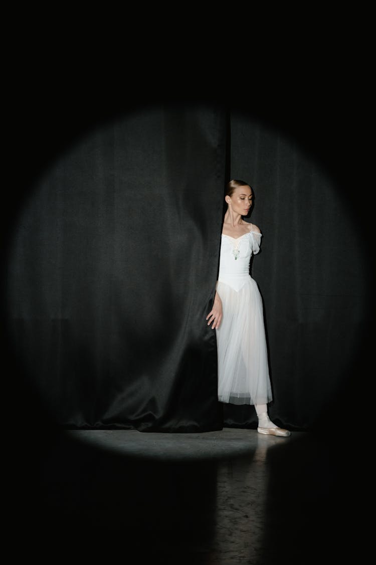 Spotlight On A Woman In White Dress Behind Black Drapes