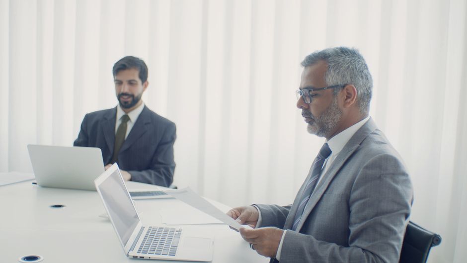 Dos colegas en un entorno corporativo, trabajando en laptops y documentos.
