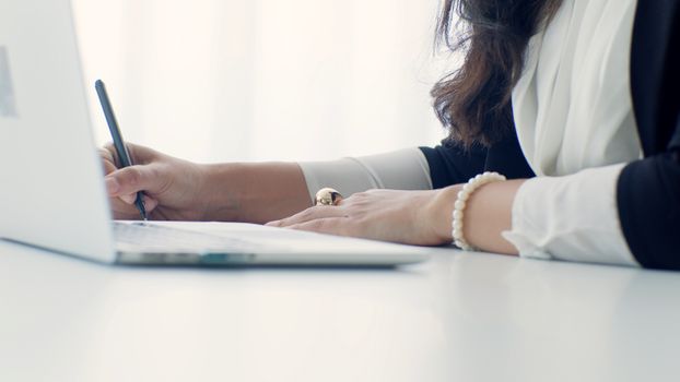 A professional woman writing at her desk in an office setting, showcasing elegance and focus.