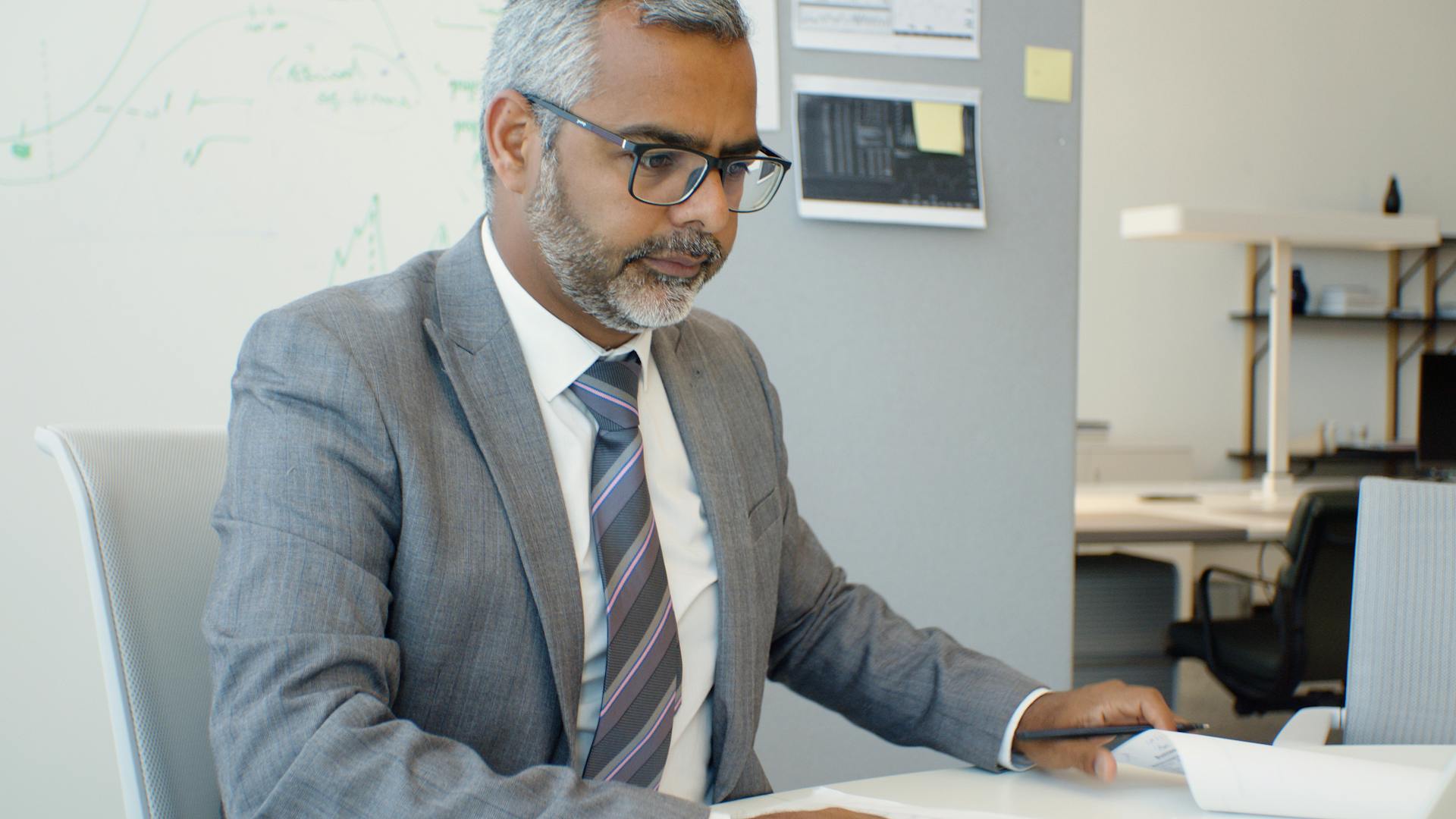 Asian man in corporate attire working at a desk in an office setting.