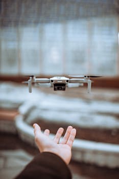 A compact drone hovers closely over an outstretched hand in a modern indoor setting, offering a technological viewpoint.