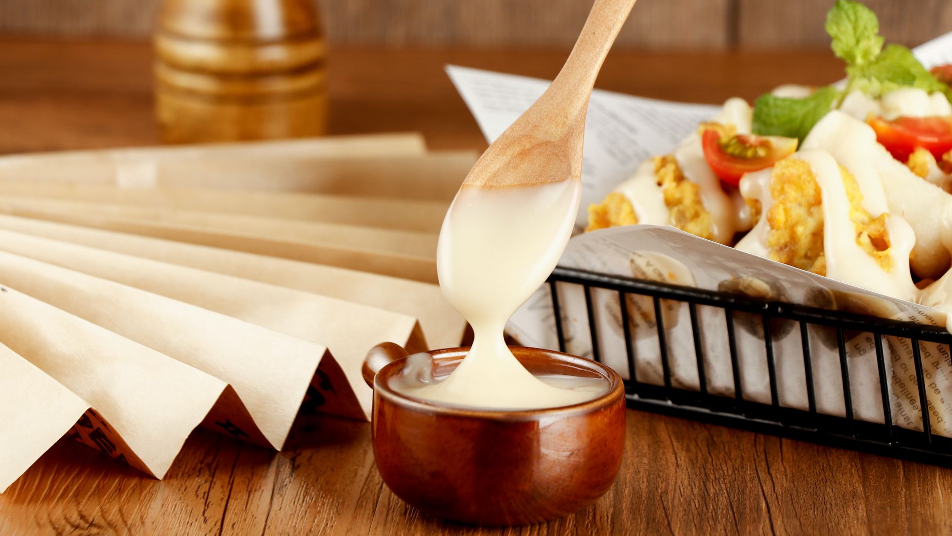 Close-up of creamy cheese sauce drizzling on crispy chicken served with cherry tomatoes in a rustic setting.