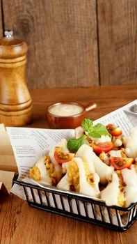 Vertical shot of crispy tacos in a basket topped with fresh tomatoes and sauce.