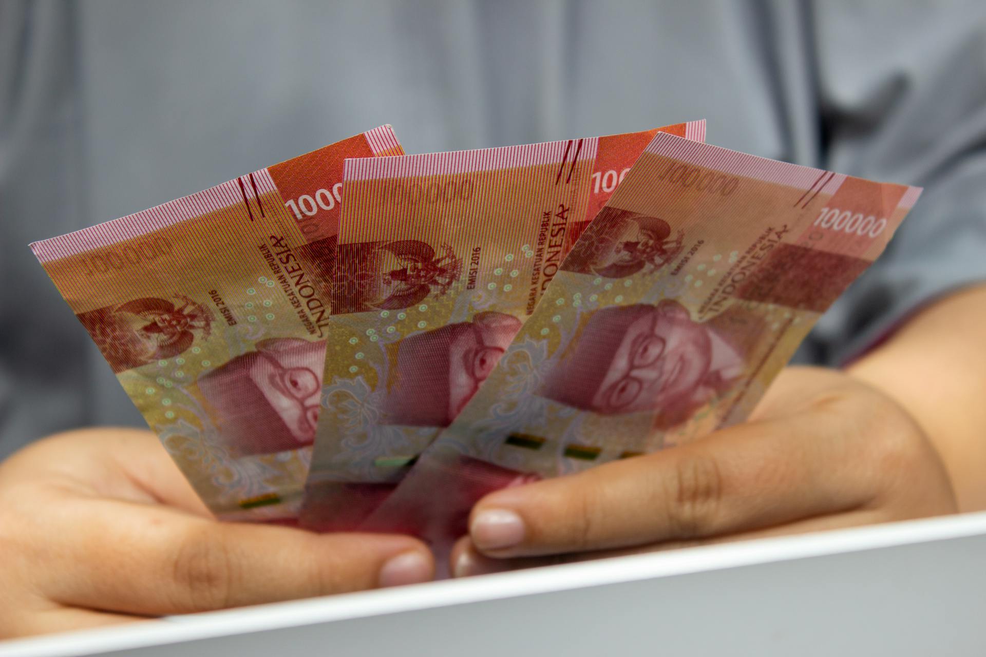 Hands holding multiple Indonesian Rupiah banknotes, showcasing currency details.