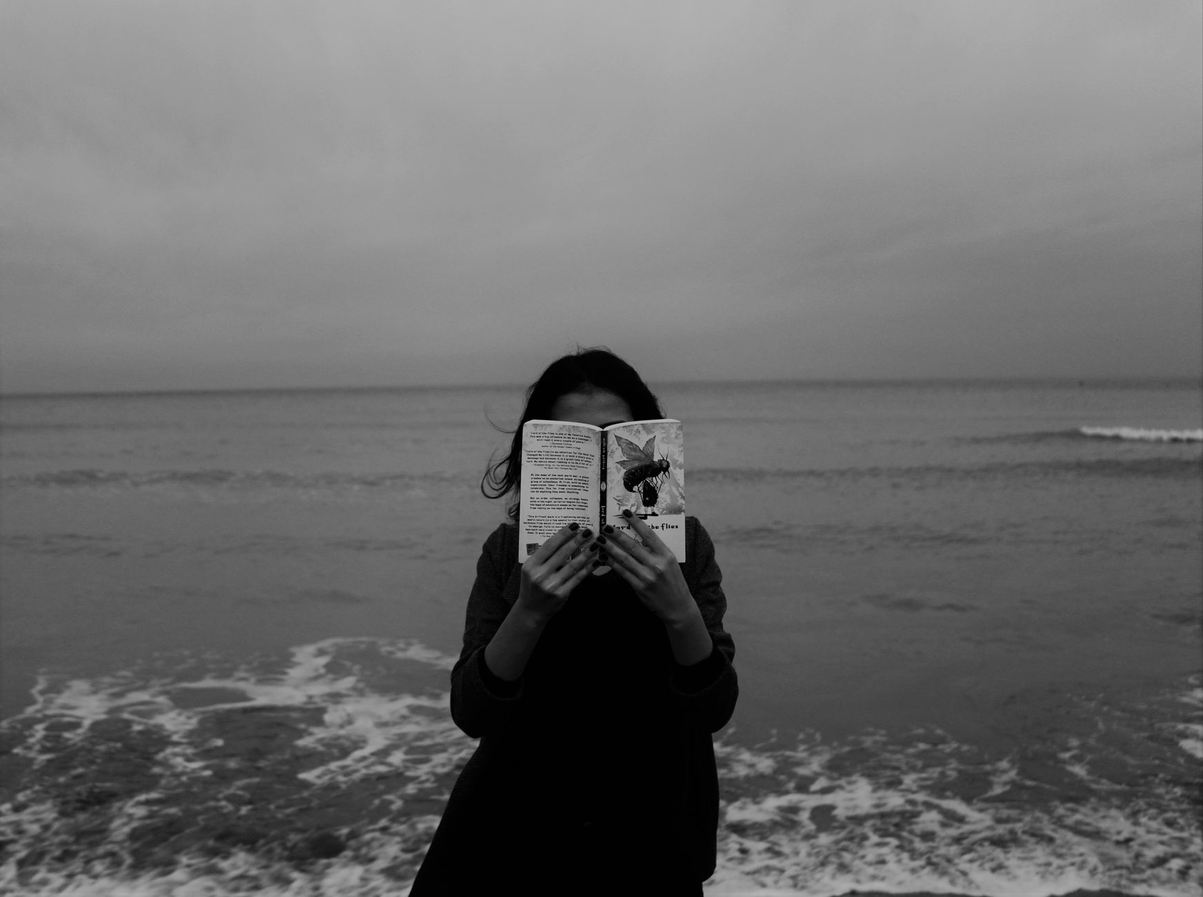 A woman reads a book by the ocean, capturing a serene moment against the seascape.
