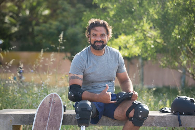 Man Wearing Elbow And Knee Pads Sitting On Concrete Bench