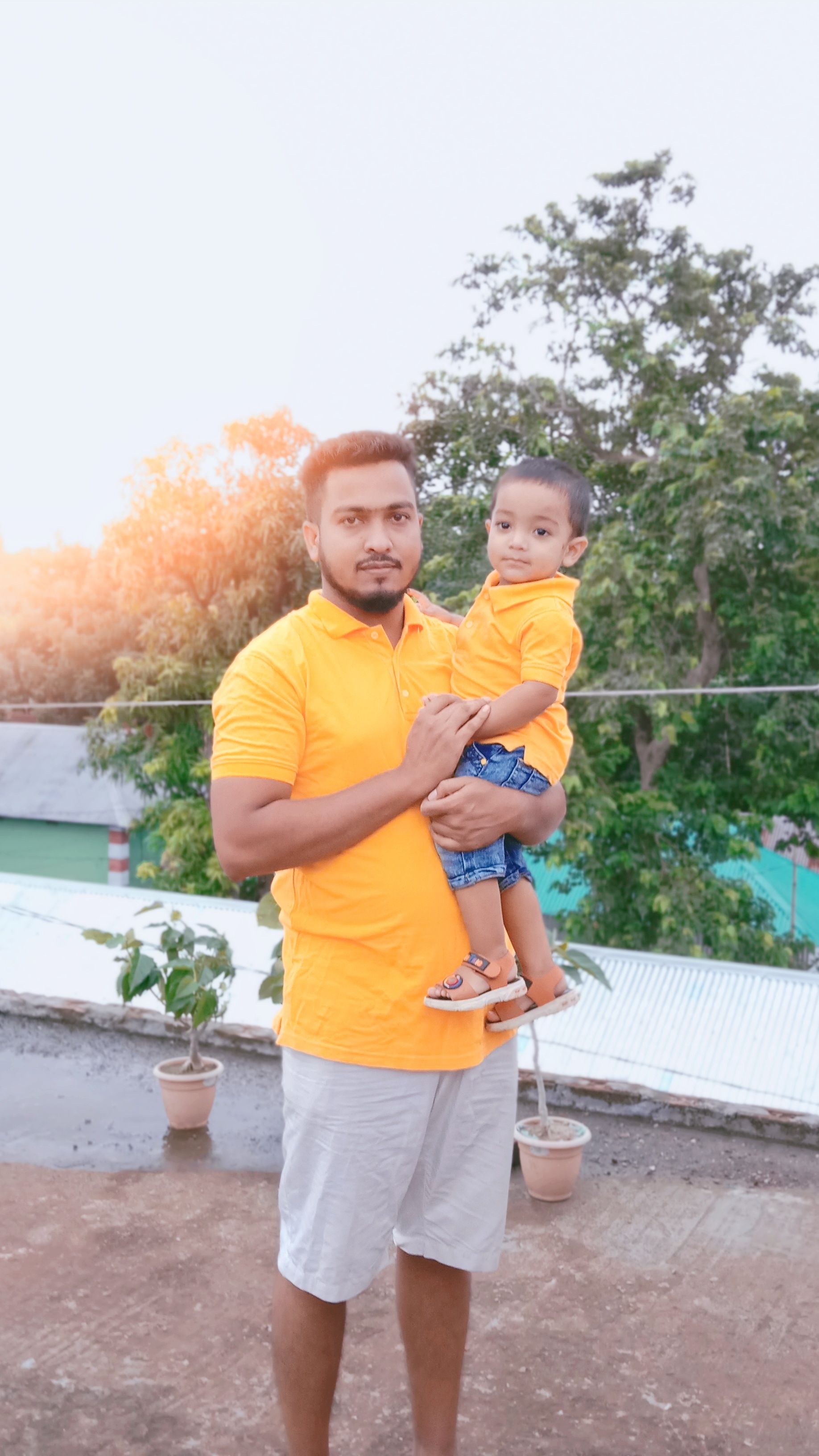 A father holding his son outside, both wearing matching yellow shirts, enjoying quality time together.