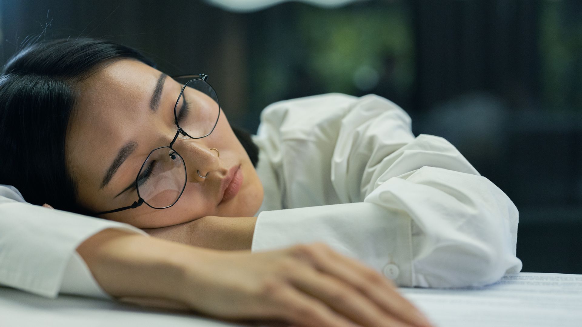 modafinil for narcolepsy: Guide A tired woman with eyeglasses sleeps on a desk indoors, highlighting exhaustion — modafinil for narcolepsy