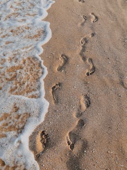 Coastal footprints on sandy beach with gentle waves, evoking peacefulness and travel vibes.