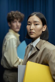 Two professionals with folders stand in an office environment, portraying teamwork and readiness.