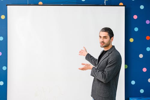A Man in Gray Blazer Standing Beside the White Board