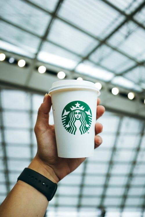 Free A hand holding a disposable coffee cup inside a bright atrium space. Stock Photo