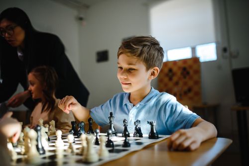 Free A young boy playing chess indoors, focusing on strategy and fun with peers. Stock Photo