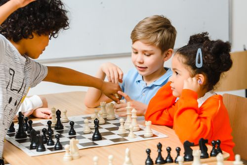 Free Group of diverse children engaged in a chess game, enhancing strategy skills. Stock Photo