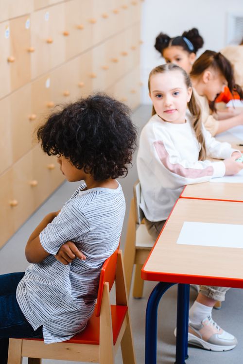 Free Children in a classroom, some interacting, while one appears upset, highlighting diverse emotions. Stock Photo