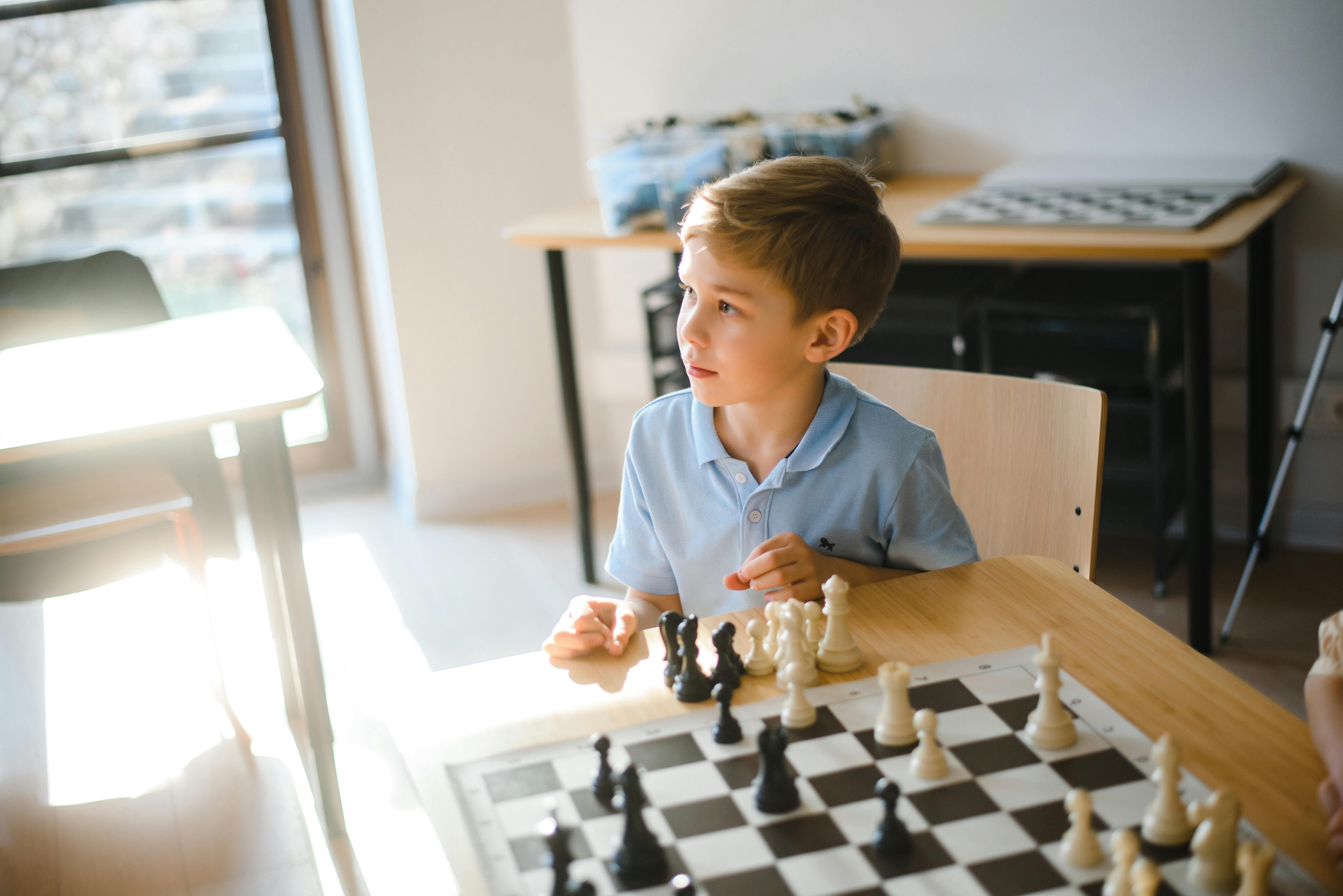 Premium Photo  Young white child playing a game of chess on large chess  board chess board on table in front of school boy thinking of next move