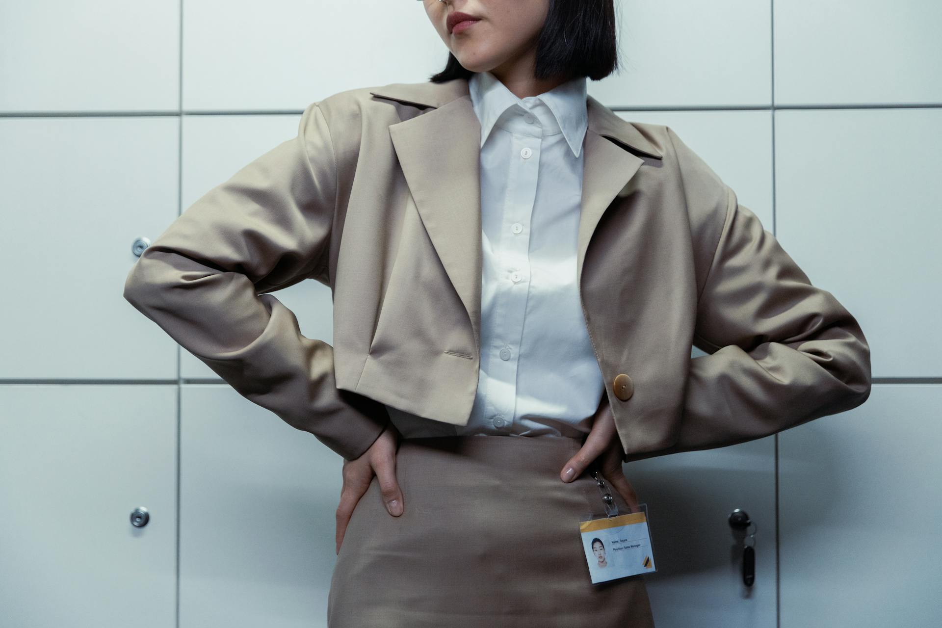 Close-up of a businesswoman with hands on waist, wearing ID badge and blazer.