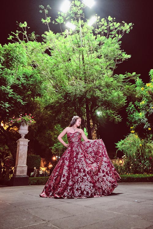 A Woman in Red Floral Gown Standing Near the Green Trees