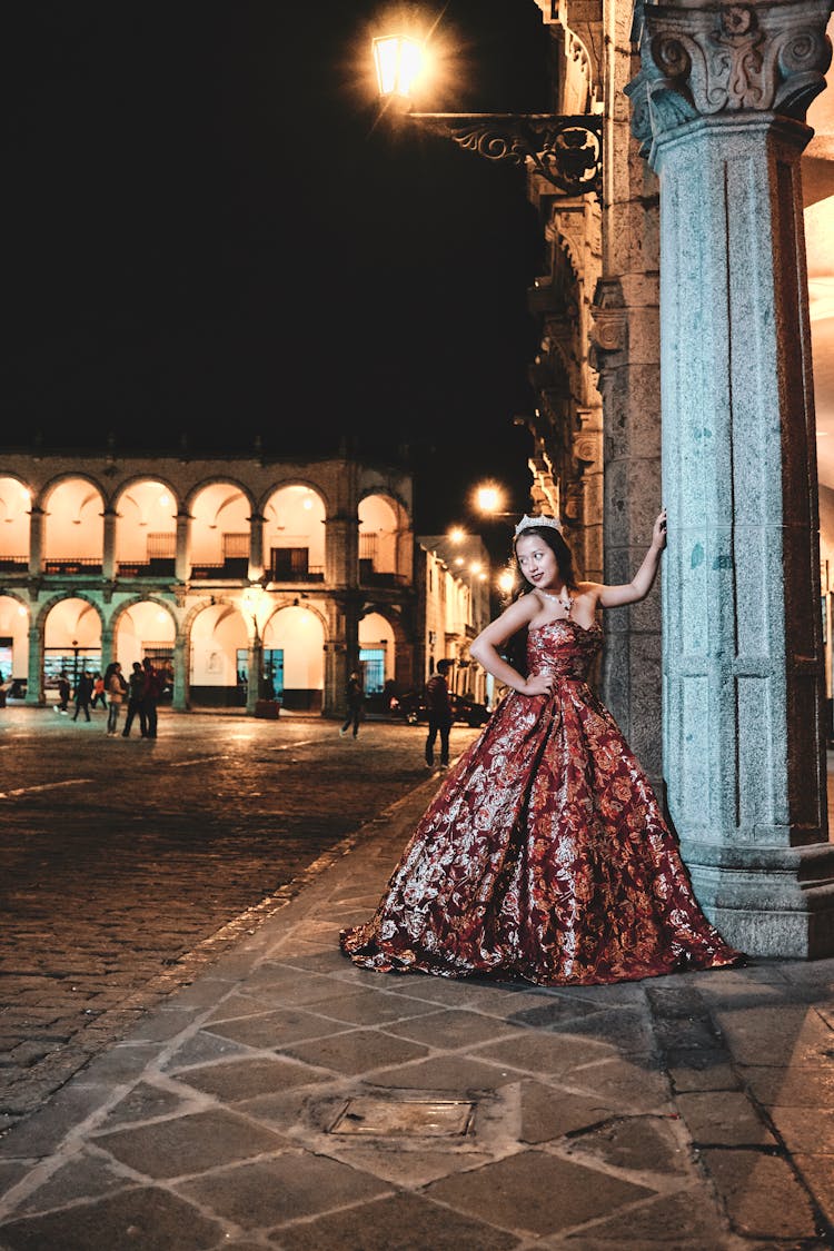 Woman In Red Shining Dress Posing Near Pillar 