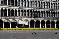 Arched windows and yellow chairs line a historic Venetian building facade.