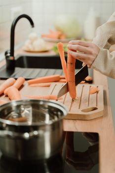 A person slicing carrots on a wooden cutting board in a modern kitchen setting.