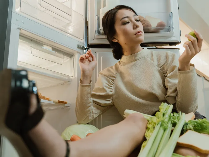 Woman sitting beside an open refrigerator with fresh vegetables Woman sitting beside an open refrigerator with fresh vegetables