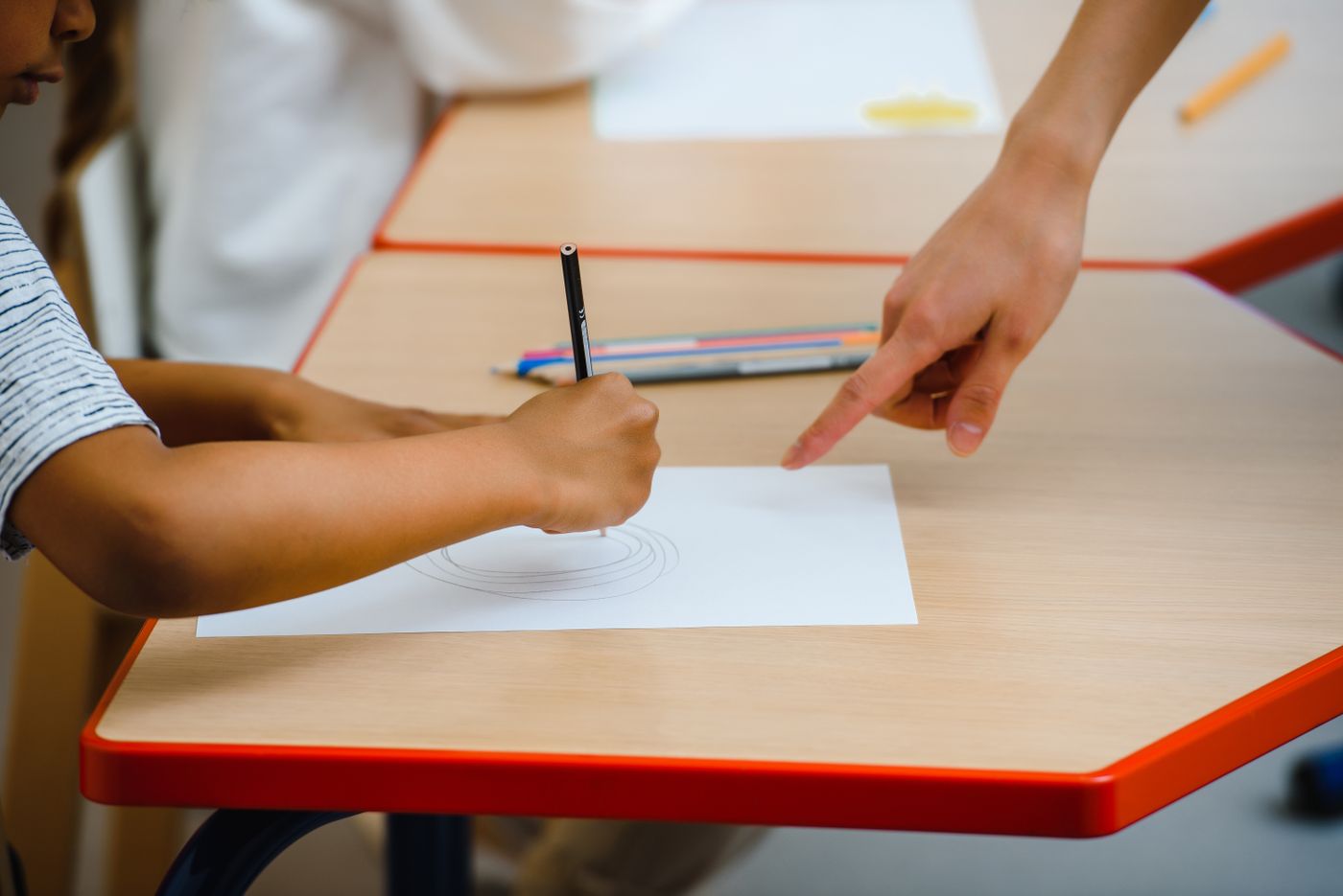 Criança a desenhar com lápis de cor, acompanhada por uma adulta