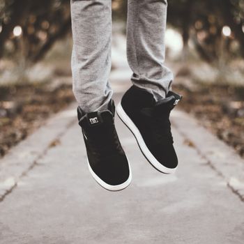 Close-up of a person jumping with black sneakers in a blurred outdoor park setting.