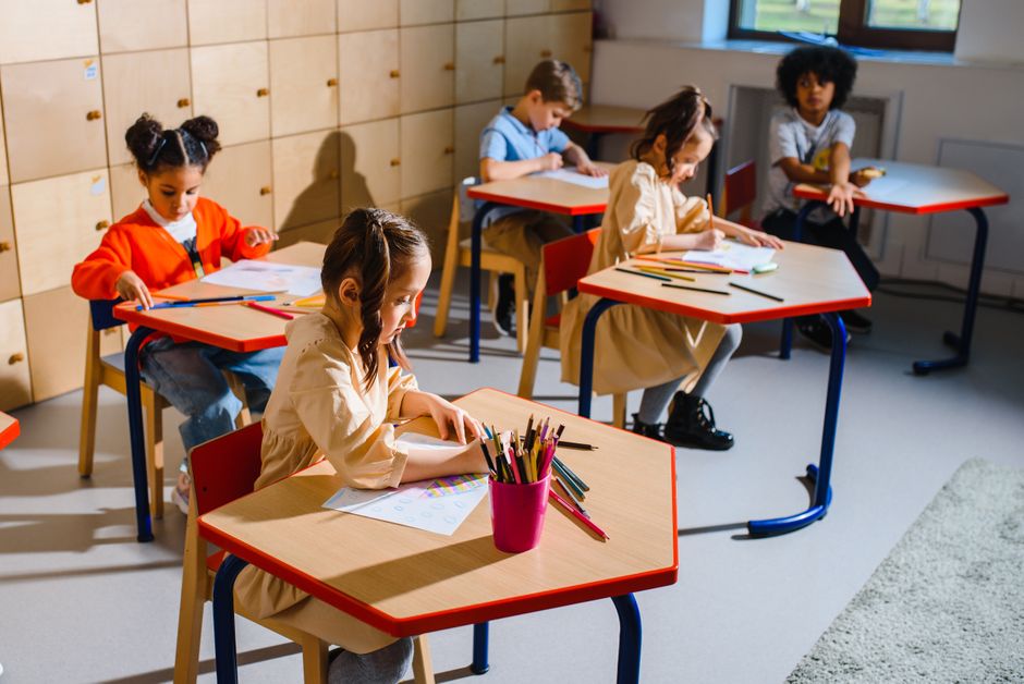 A group of diverse children sitting in a classroom, actively learning and drawing at their desks.