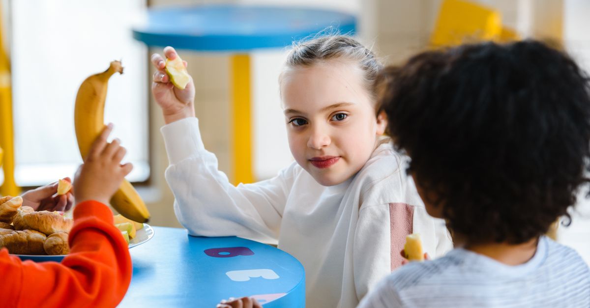 A diverse group of elementary students eating a healthy, colorful lunch together in a bright cafeteria