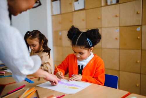 Free Children engage in creative drawing activities with teacher assistance in a vibrant classroom setting. Stock Photo