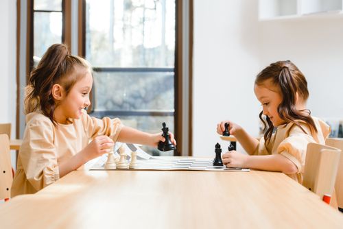 Free Two young girls playing chess with focus and joy indoors on a sunny day. Stock Photo