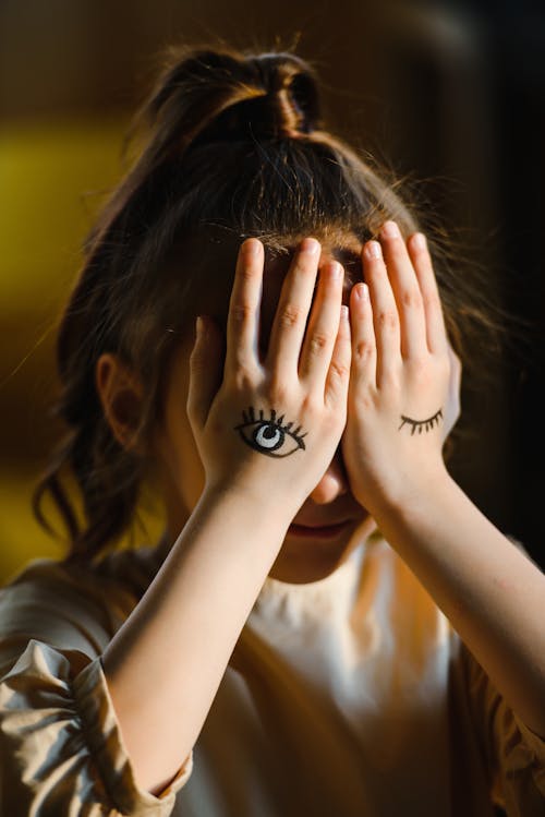 A Young Girl Covering Her Face with Drawing on Her Hands