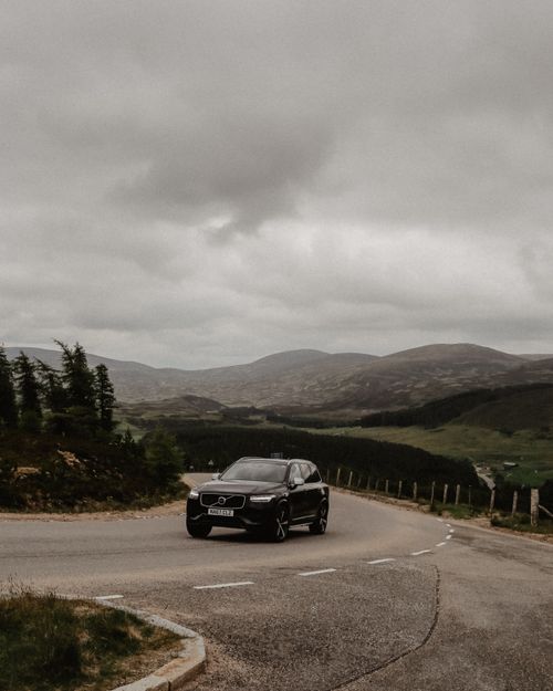 Free A Volvo SUV navigating a winding road in the misty, scenic Scottish Highlands with cloudy skies. Stock Photo