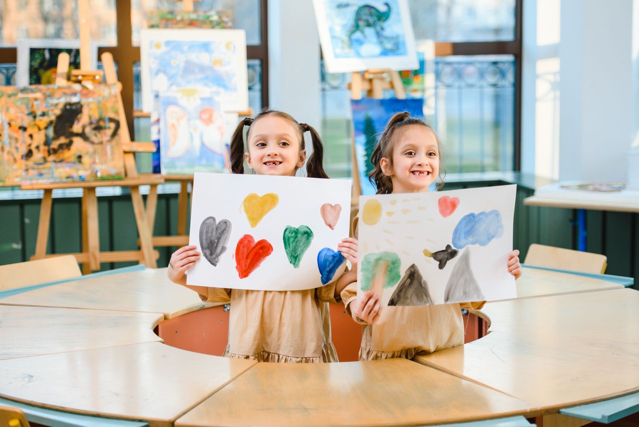 Dua anak menunjukkan lukisan warna-warni di kelas seni