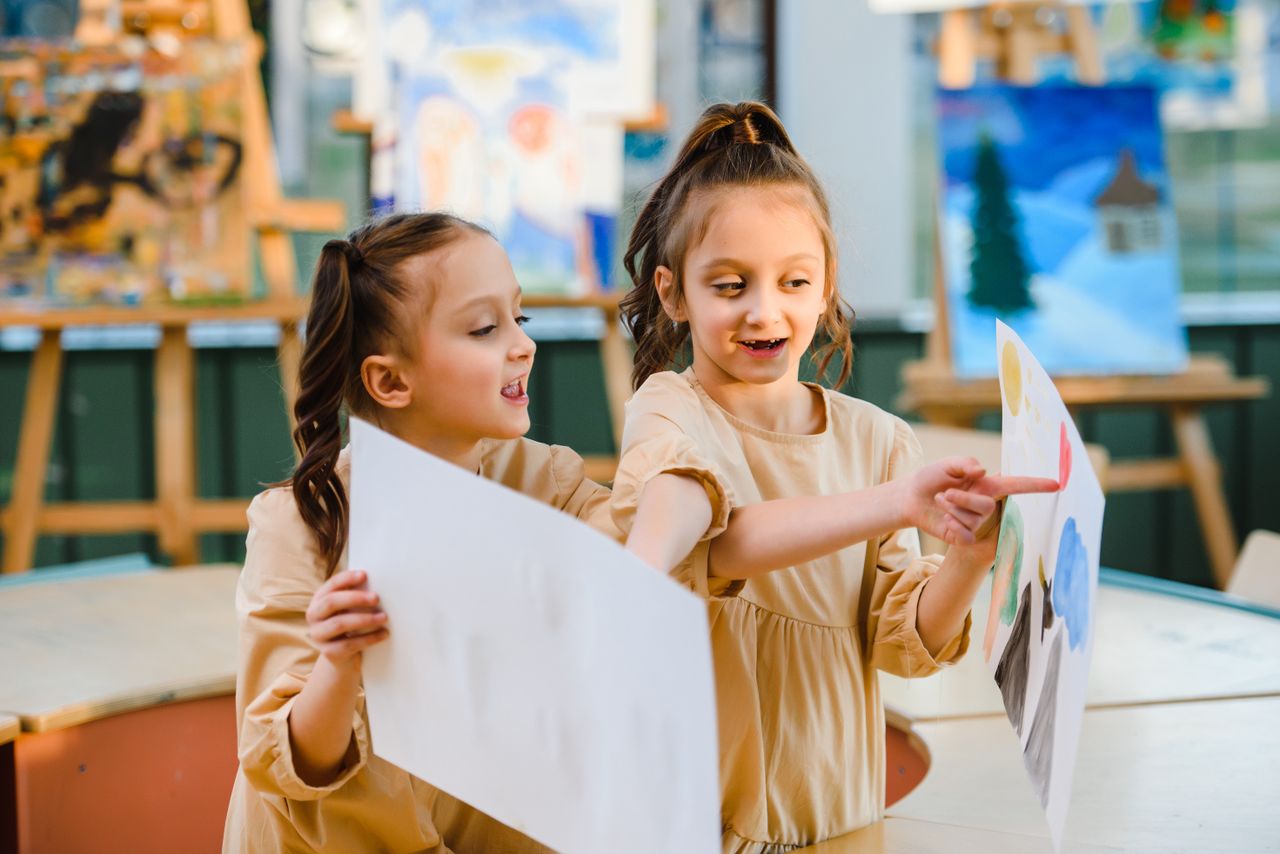 Dua anak perempuan sedang berbagi dan mendiskusikan lukisan mereka di kelas seni